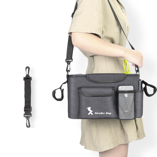 Person carrying a black stroller bag with multiple pockets and a strap attachment on a white background