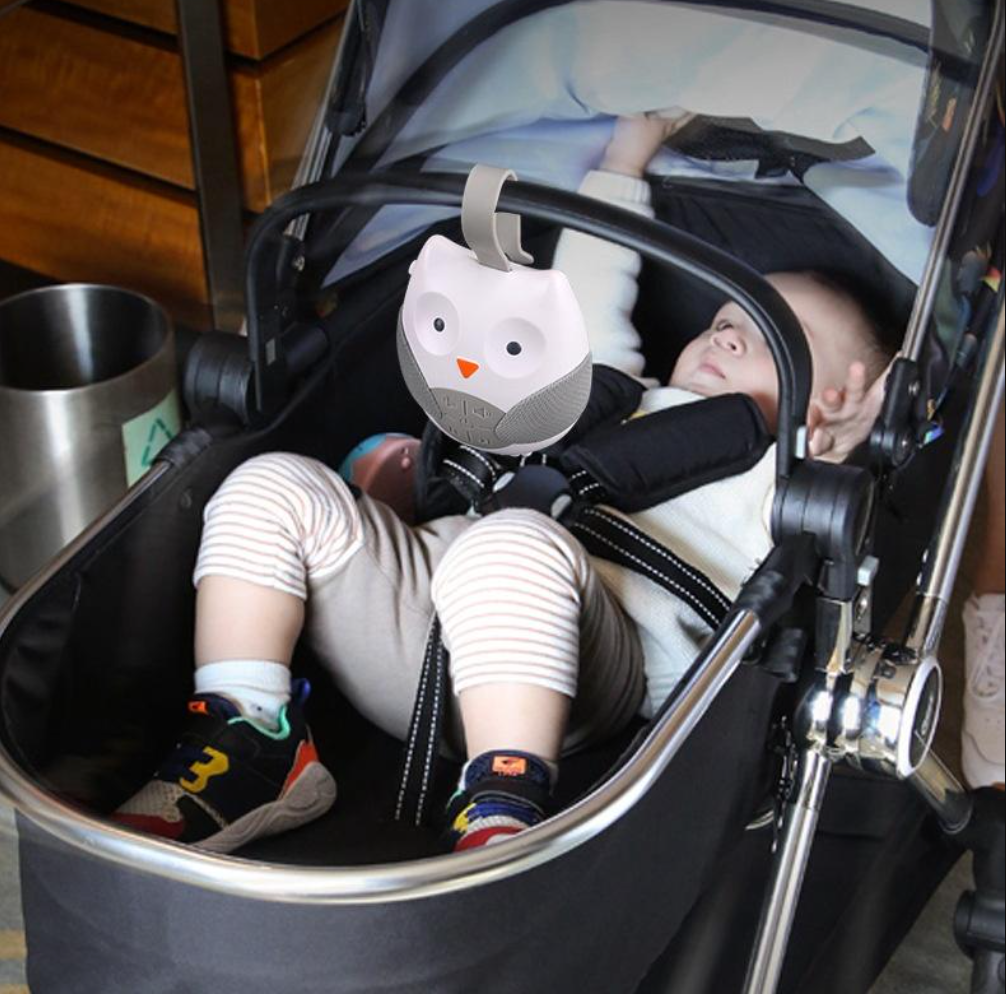 Baby in a stroller with a toy owl attached, sitting in the strollee